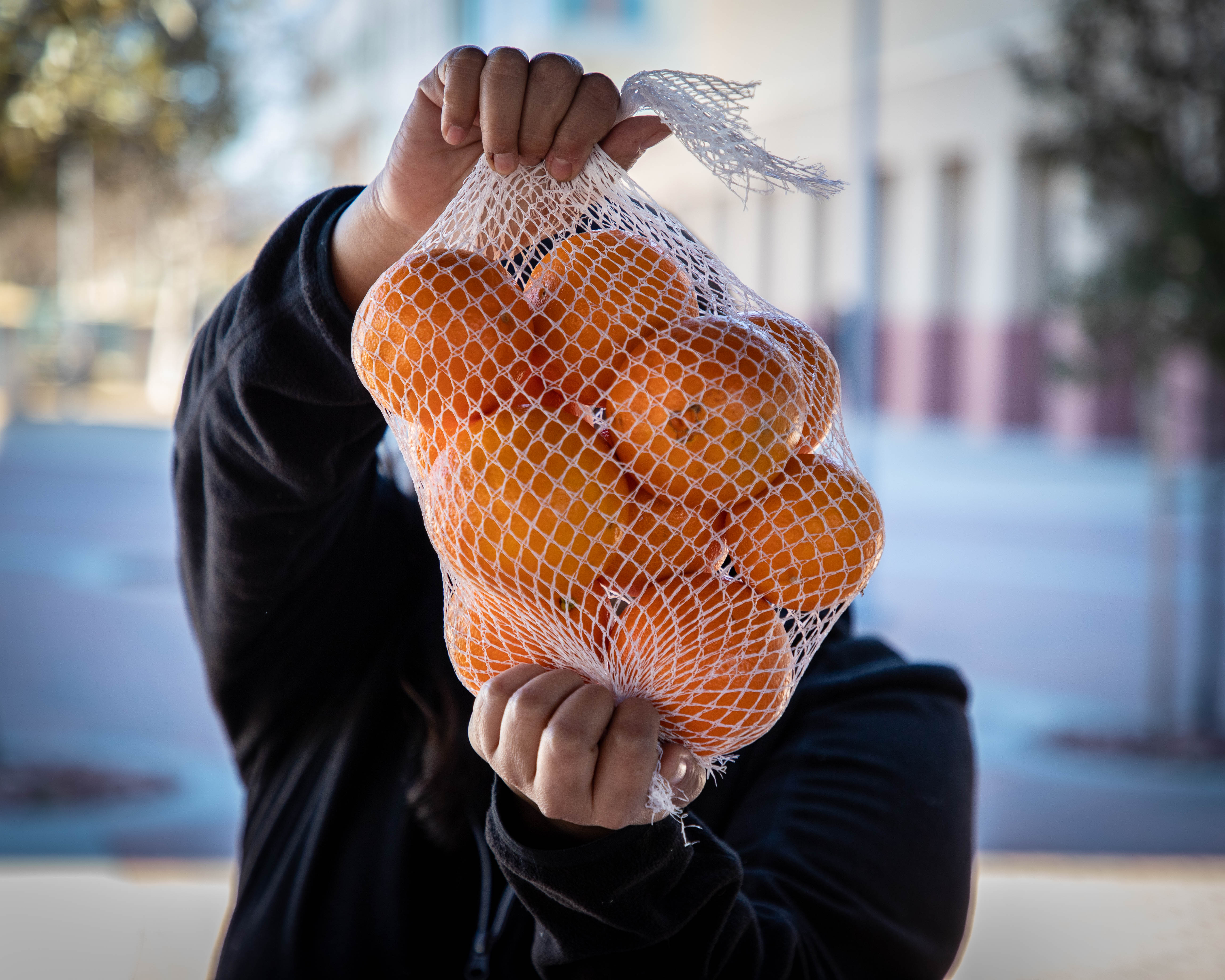 student holding bag of oranges, covering face